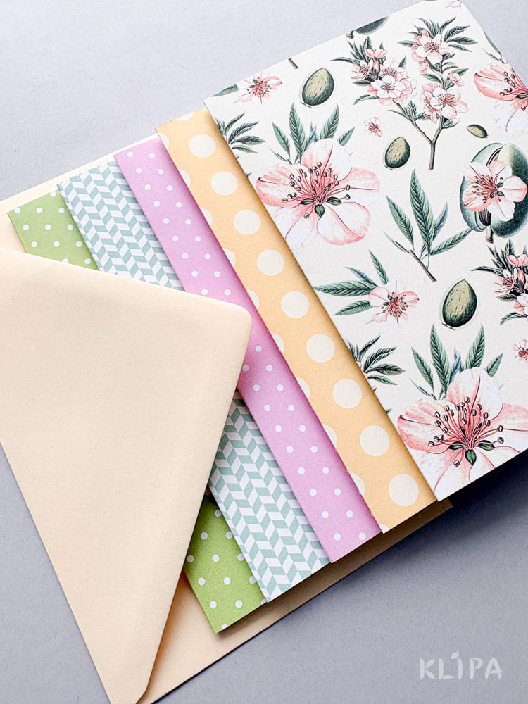 Assorted pastel patterned craft papers and envelopes fanned out for scrapbooking or gift wrapping, including florals and polka dots.