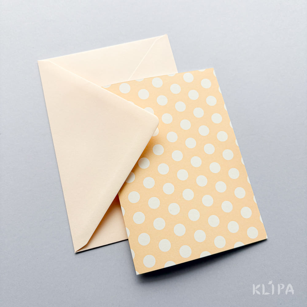 Beige envelope partially tucked under a peach-colored polka-dot card on a light gray background.