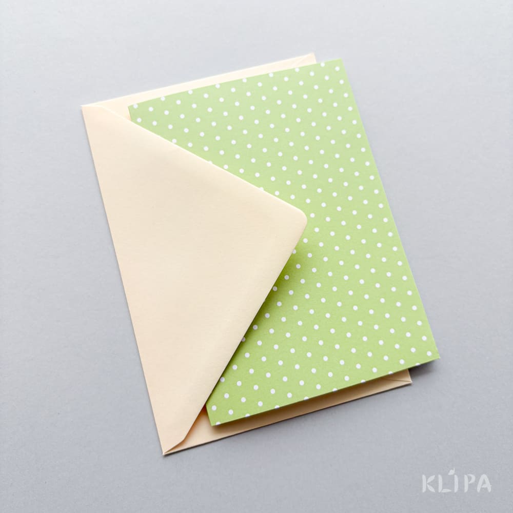 Flat lay of two pastel stationery cards: a cream envelope partially tucked under a light green polka-dotted card on a gray background